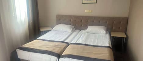 Habitación de hotel con cama doble, dos mesitas de noche, cabecero y un cuadro enmarcado en la pared.