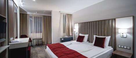 A hotel room with a large bed, a desk, a chair, a small table, a TV, and a mirror.