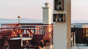 A terrace with round tables and chairs, a railing, and decorative items on a pillar.