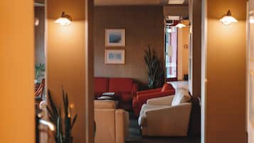 A hotel lobby with a red sofa, beige armchairs, and two framed pictures on the wall.