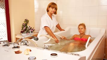 A bathtub with multiple controls and a person standing beside it.