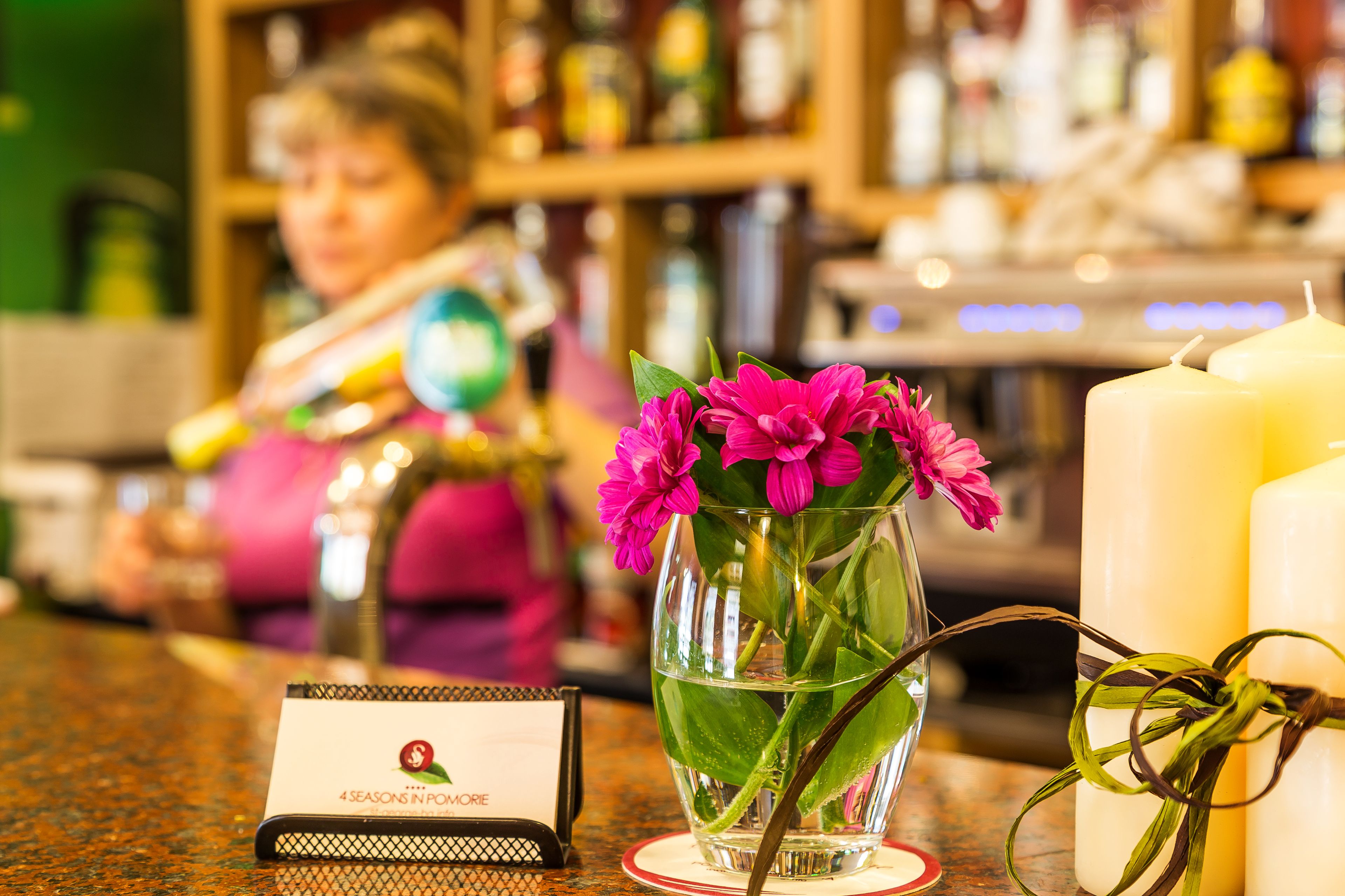 Un área de bar con un florero de vidrio con flores rosadas, una vela y un atril para el menú.