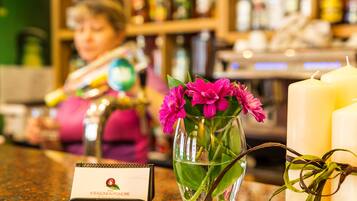 Un área de bar con un florero de vidrio con flores rosadas, una vela y un atril para el menú.