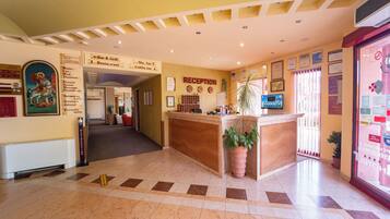 A hotel reception area with a reception desk, directional signs, and a wall-mounted display.