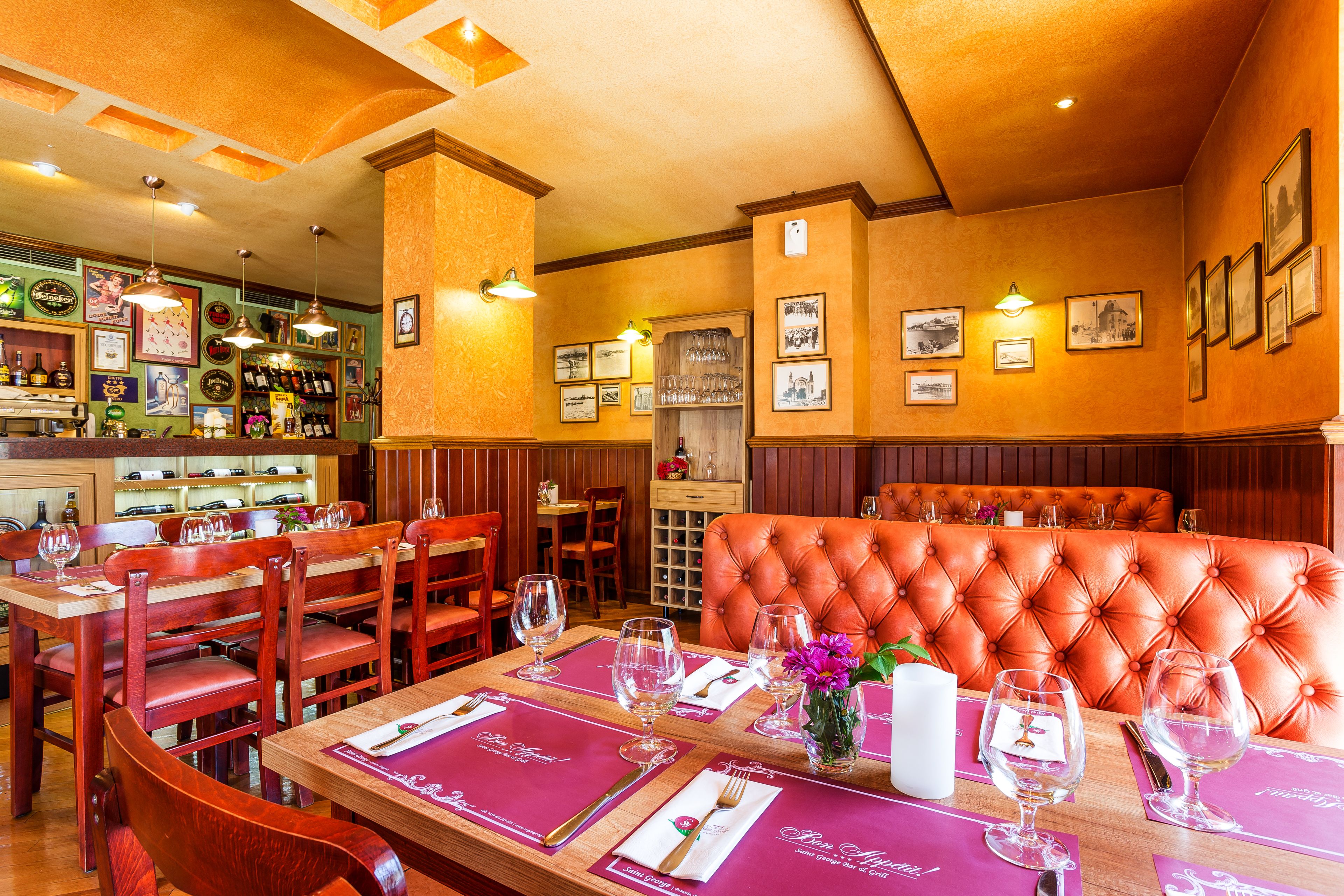 Un interior de restaurante con mesas de madera, asientos tapizados en rojo y una zona de bar con botellas de licor.