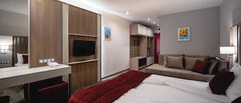 A modern hotel room with a large bed, a desk with a telephone, a TV, and a red blanket.