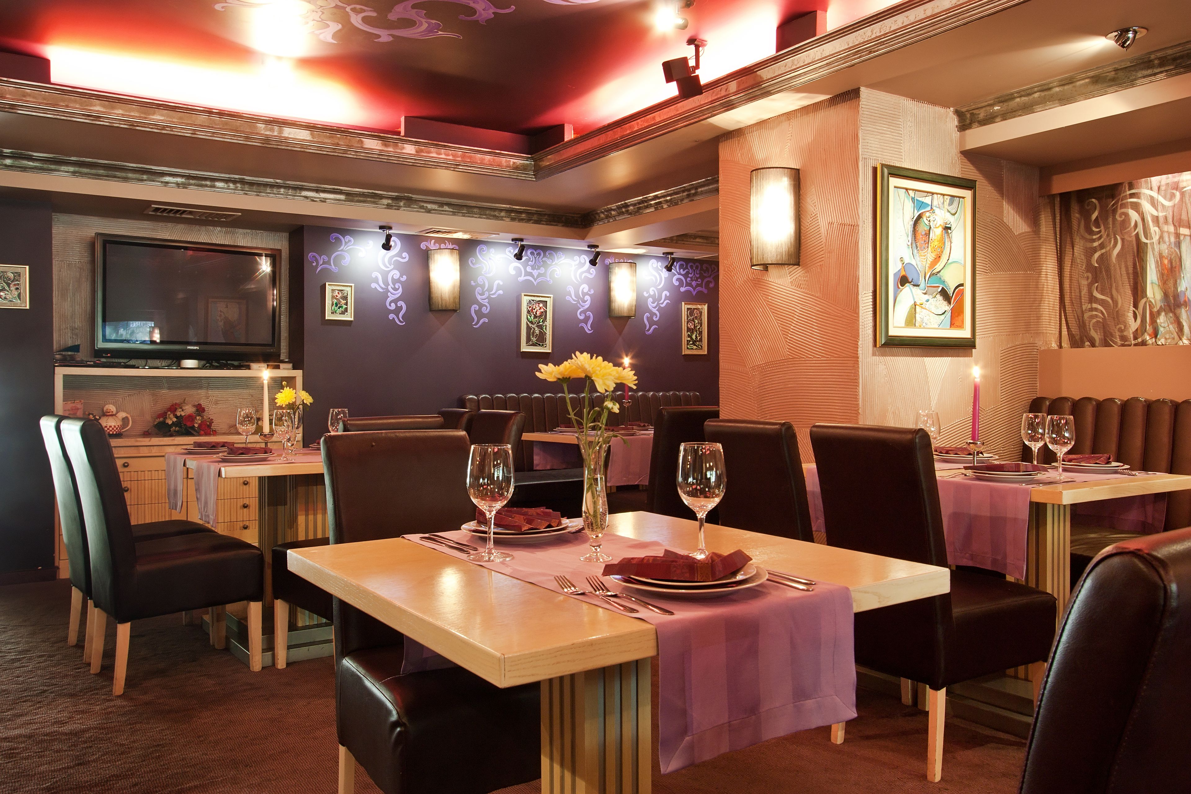 Un restaurante con mesas dispuestas para comer, un televisor en la pared y luces decorativas.