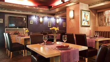 Un restaurante con mesas dispuestas para comer, un televisor en la pared y luces decorativas.