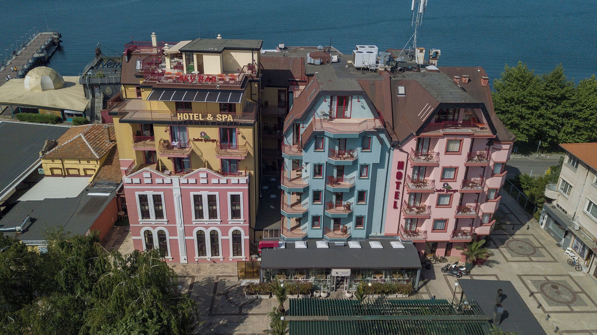A multi-story hotel with balconies, a rooftop terrace, and a view of the sea.