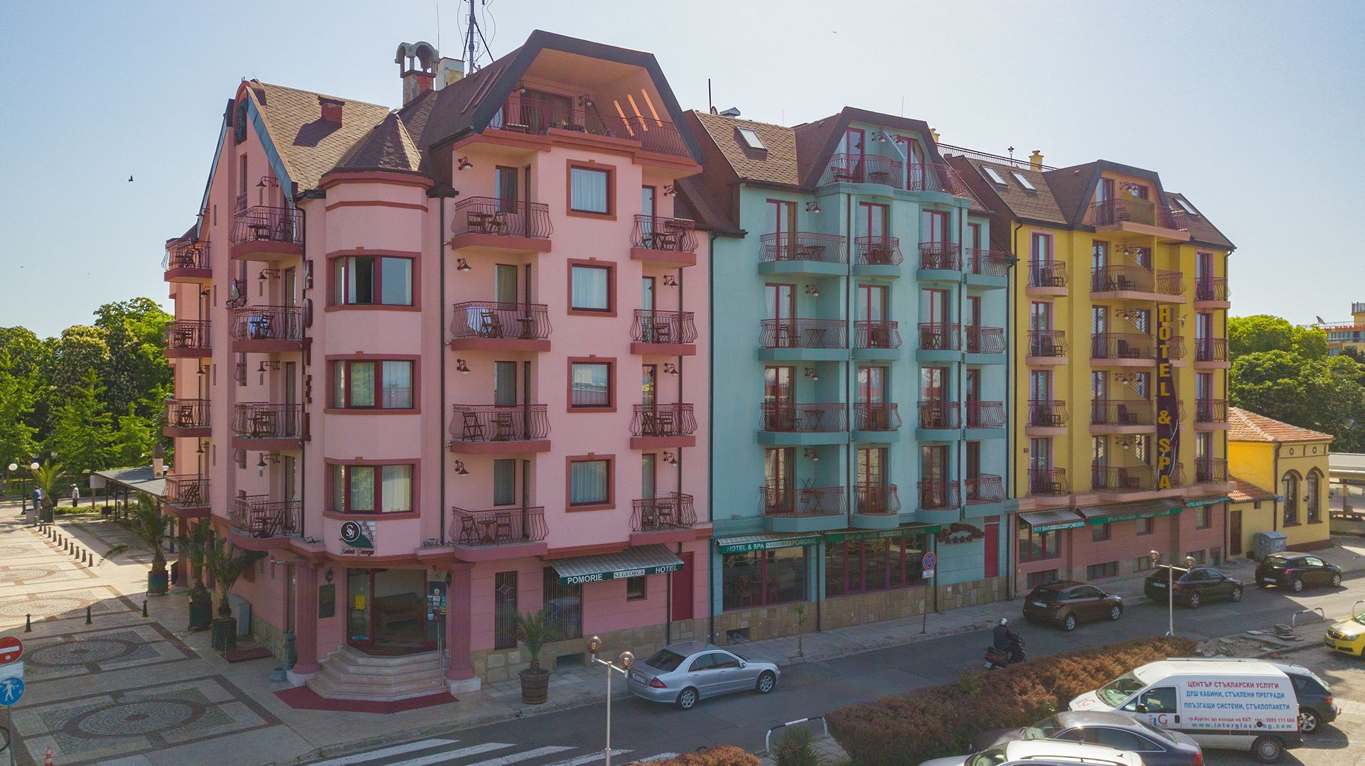 Un hotel de varios pisos con balcones, un estacionamiento y vista a la calle.