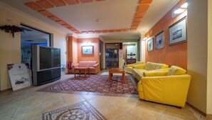 A hotel lobby with a television, sofas, a patterned rug, and a tiled floor. - Saint George Hotel & Spa (Pomorie)