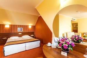 A hotel room with a double bed, bedside tables, a coffee maker, a vase of flowers, and a bathroom visible through an archway. - Saint George Hotel & Spa (Pomorie)