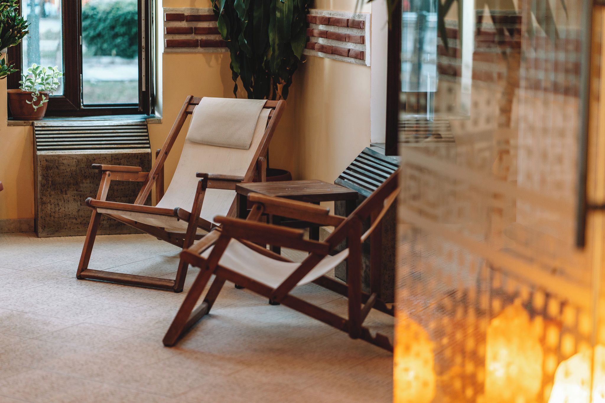 A room with two wooden lounge chairs, a small table, and a potted plant by the window.