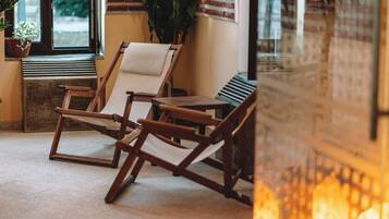A room with two wooden lounge chairs, a small table, and a potted plant by the window.