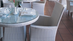 Ein Restaurant mit runden Glastischen, Korbstühlen und Topfpflanzen.
