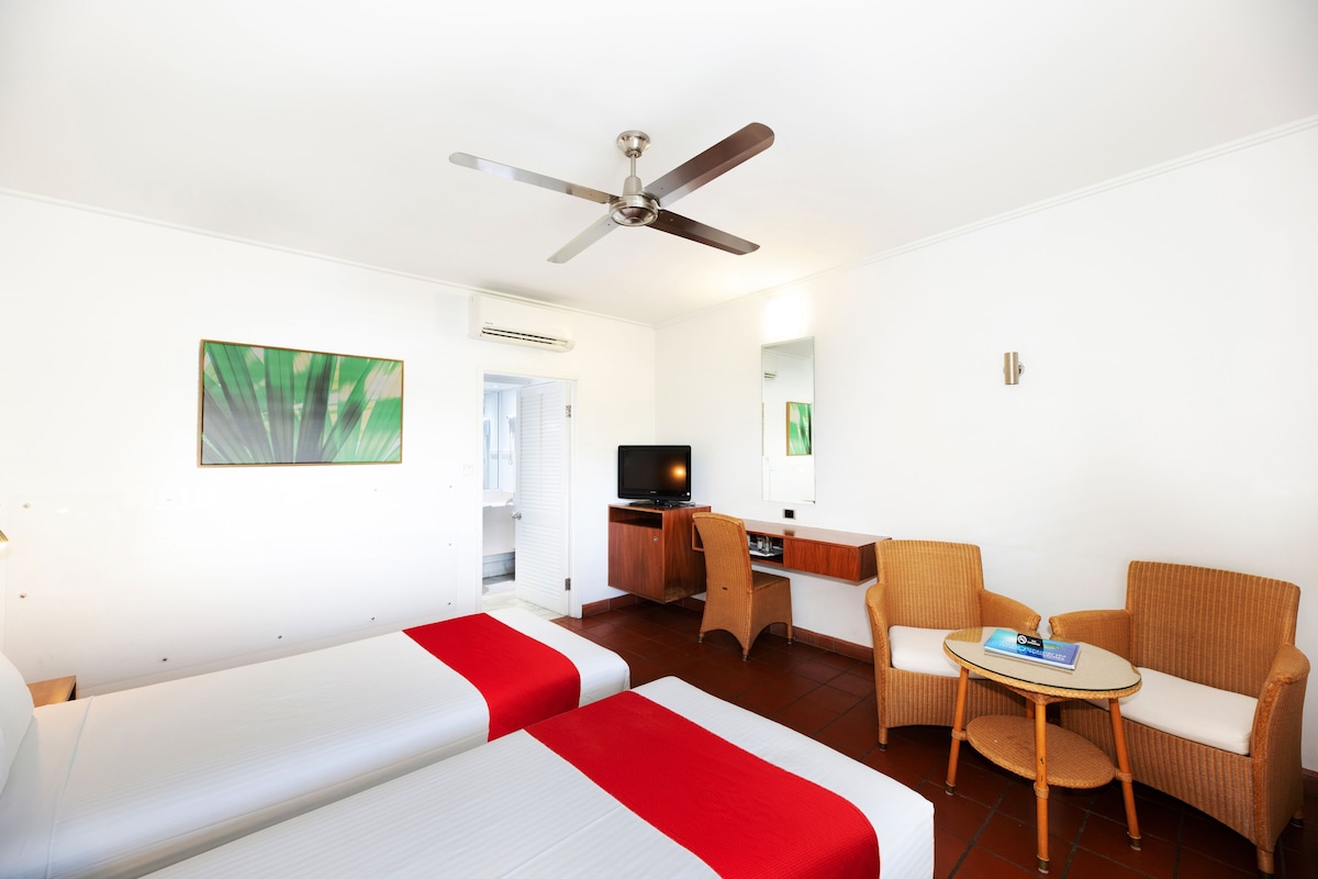 Una habitación de hotel con dos camas, un escritorio, una silla, un televisor y un ventilador de techo.