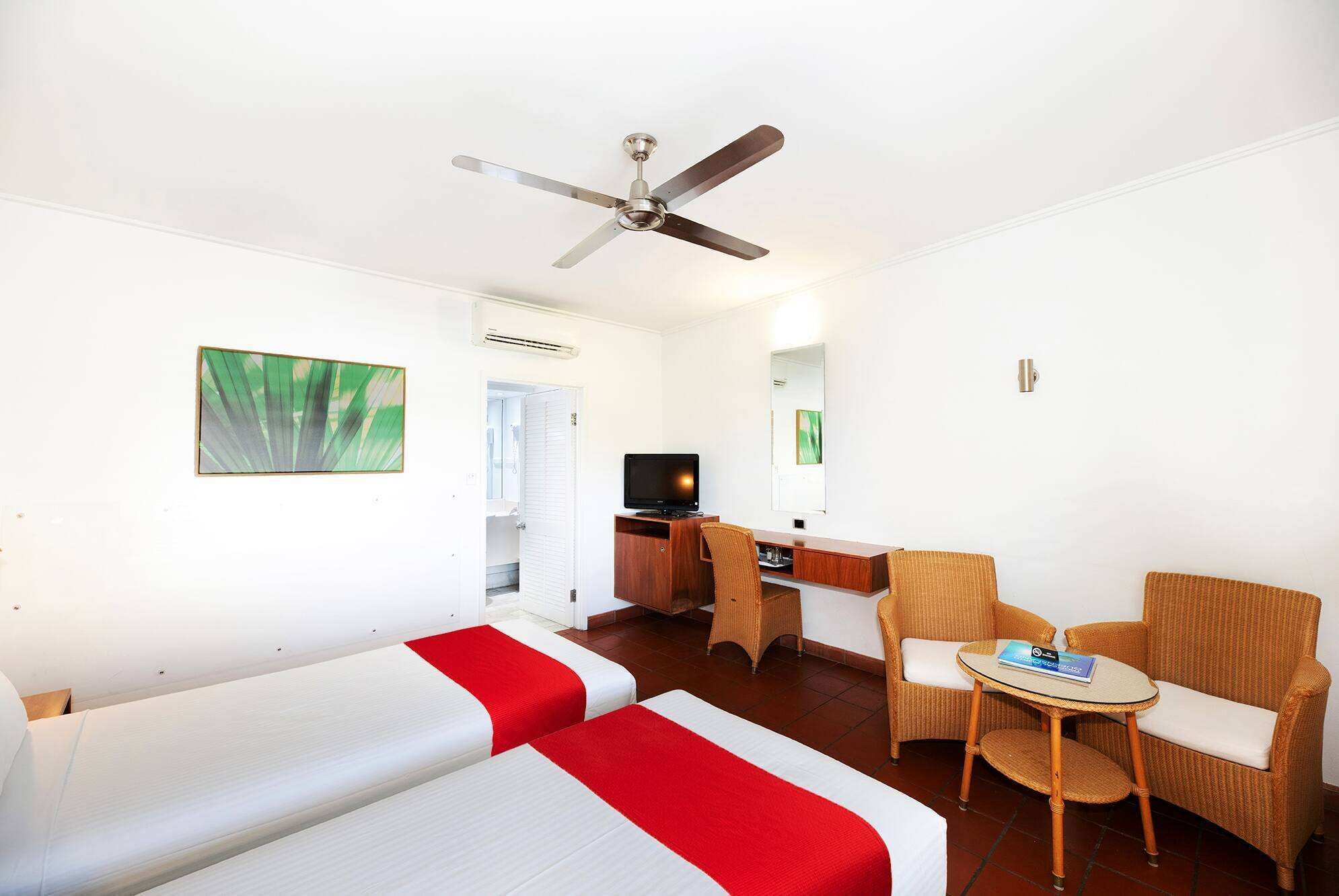Habitación de hotel con dos camas, un escritorio, televisor, una silla, una mesita y un ventilador de techo.