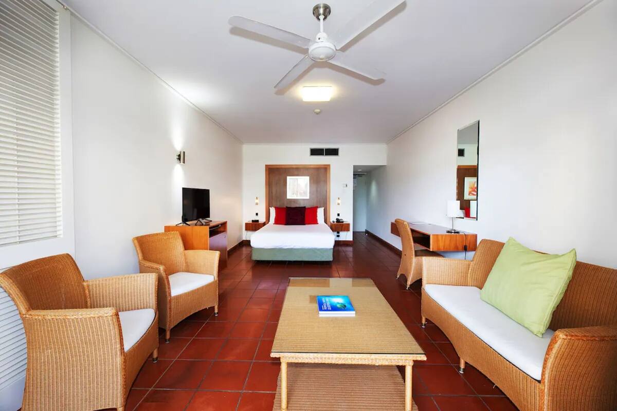 A hotel room with a bed, two wicker sofas, a coffee table, a TV, and a ceiling fan.
