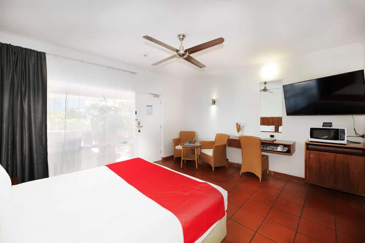 A hotel room with a bed, a desk, a chair, a television, and a ceiling fan.