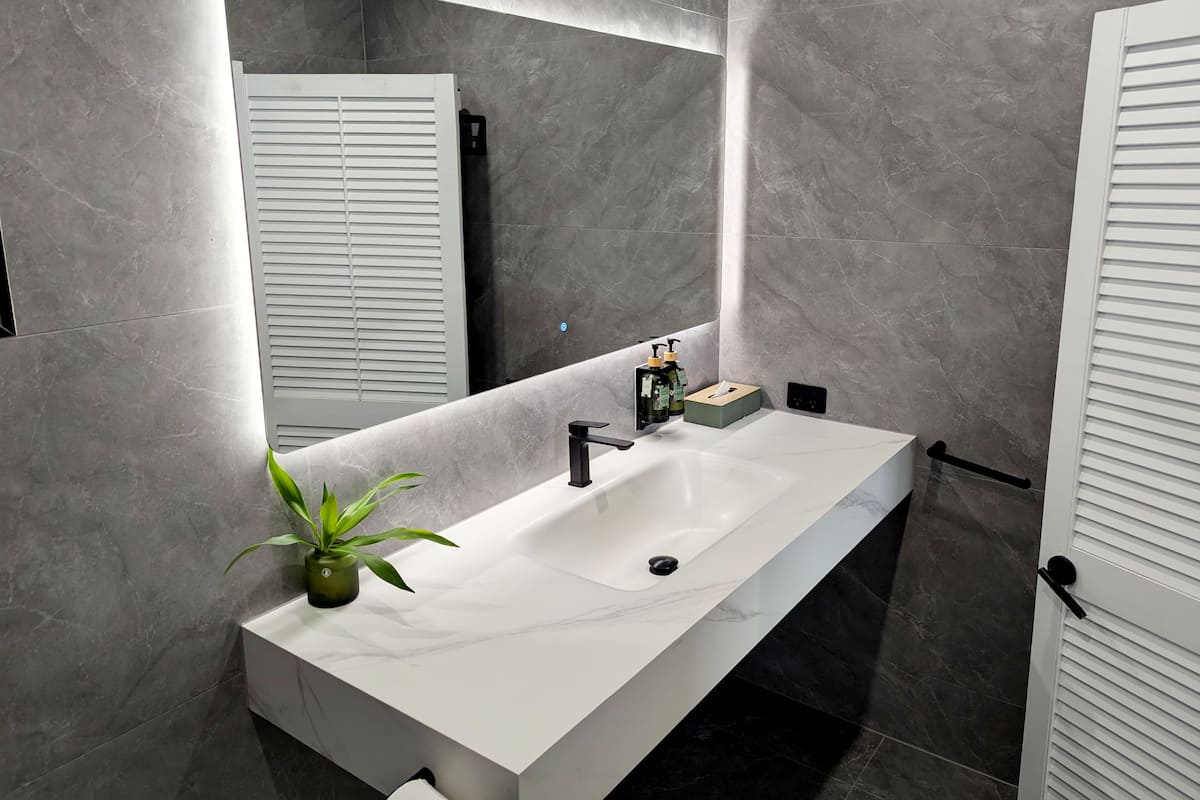 A modern bathroom with a white sink, a mirror, and a potted plant.