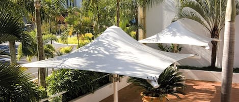 A patio area with white chairs and a table, surrounded by palm trees and a white fence.