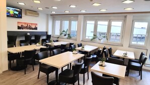 A restaurant with multiple tables and chairs, large windows, and a flat-screen TV on the wall.