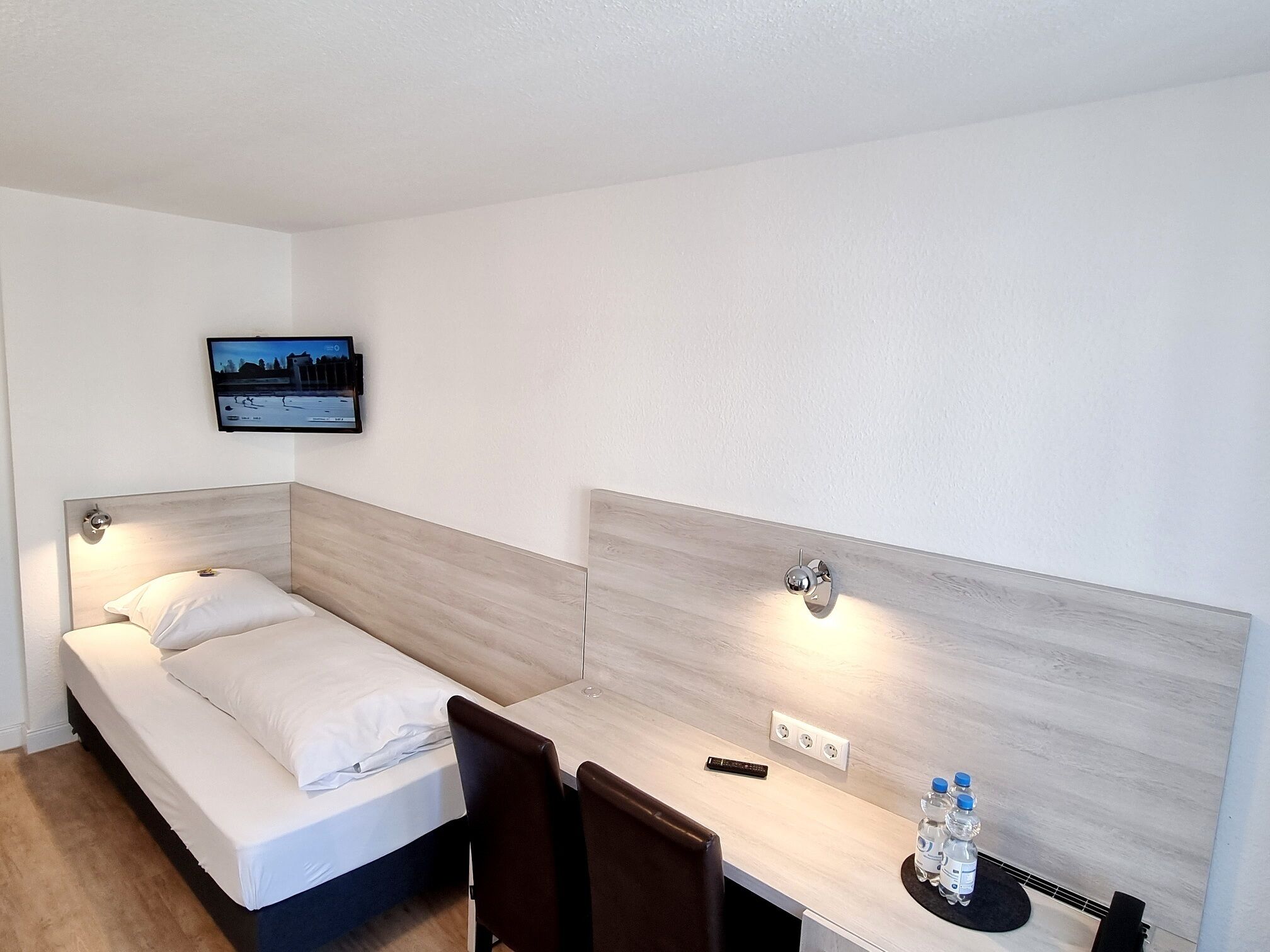 A hotel room with a bed, a desk, and a TV mounted on the wall.