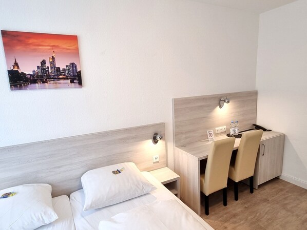 A hotel room with a bed, a desk with a chair, a nightstand, and a wall-mounted light. - Adler Hotel Frankfurt (Frankfurt)