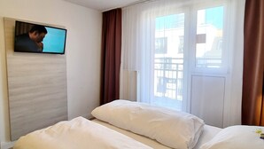 A hotel room with two beds, a television on the wall, and a window with curtains.