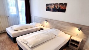 A hotel room with two beds, a wooden headboard, a nightstand, and a cityscape artwork on the wall.