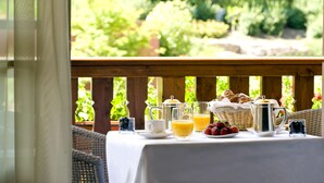 A breakfast table with a variety of food and drinks, a wicker chair, and a view of greenery. - Hostellerie des Châteaux & Spa (Ottrott)