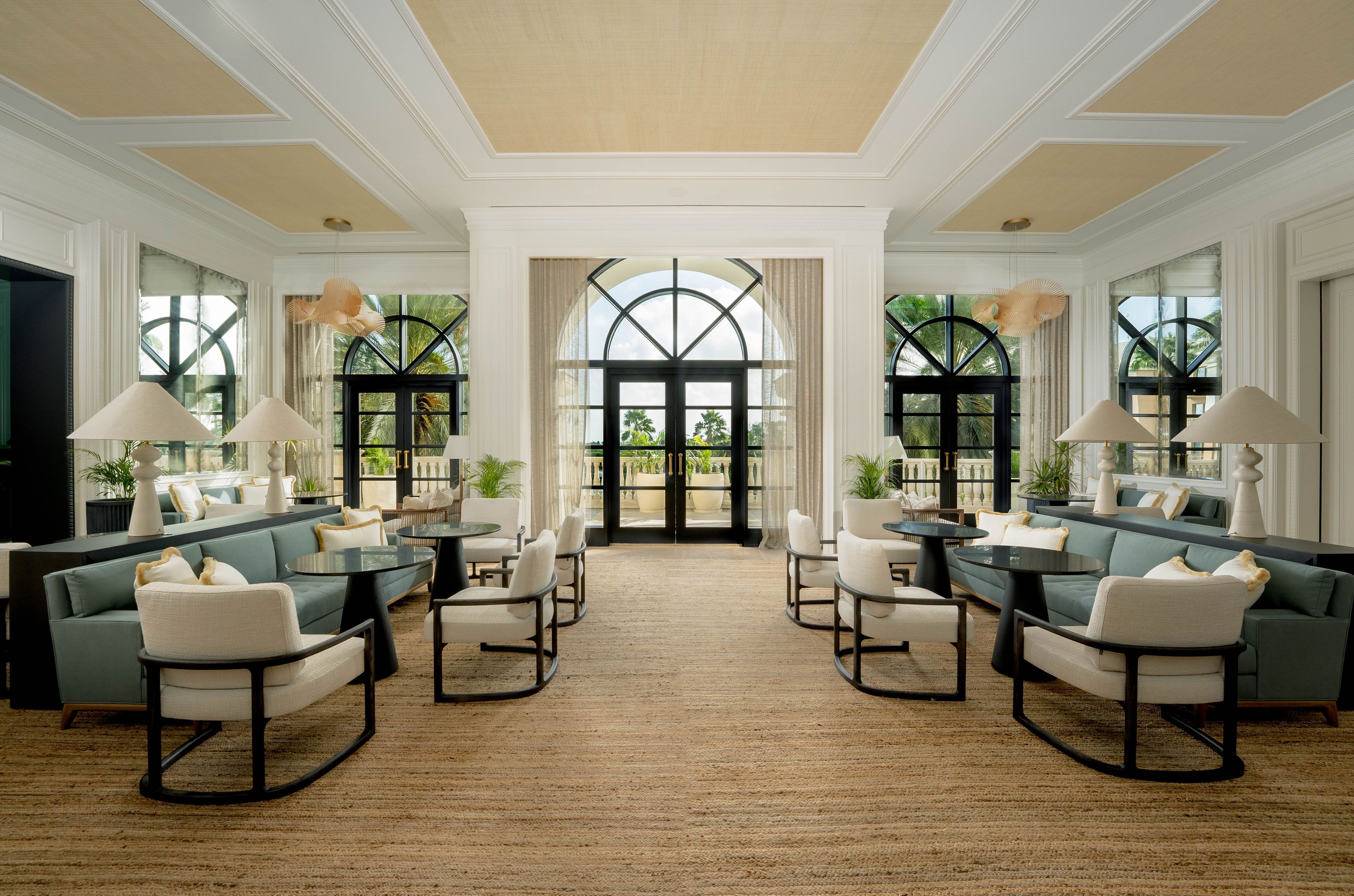 A spacious hotel lobby with a central seating area, large windows, and a view of the outdoors.