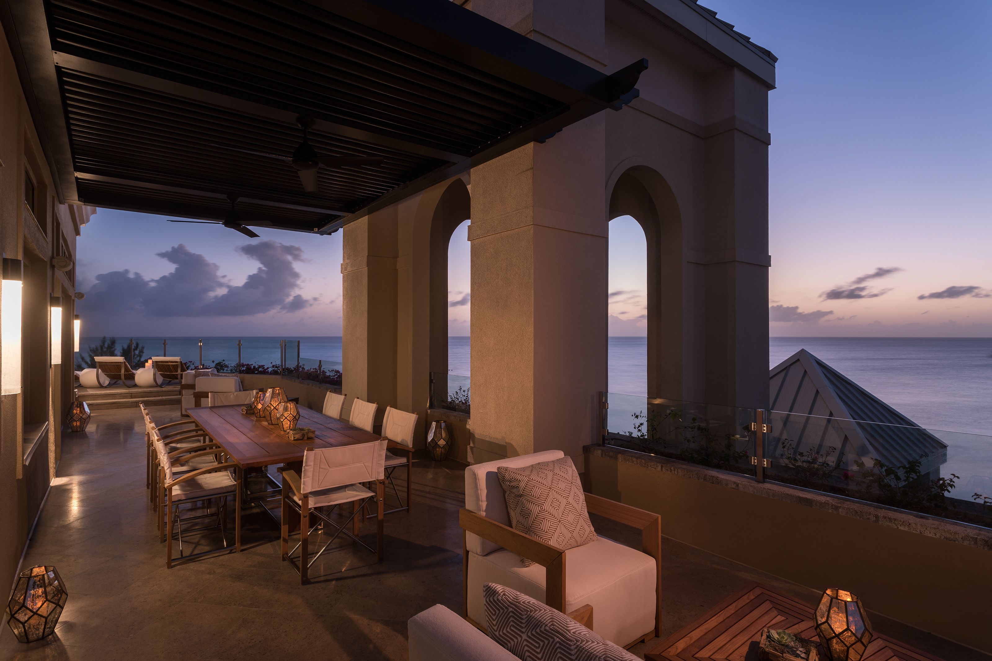 An outdoor patio with a dining table, chairs, and a sofa, overlooking the ocean.