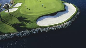 Campo de golf con búnkeres de arena, obstáculos acuáticos y un puente al fondo.