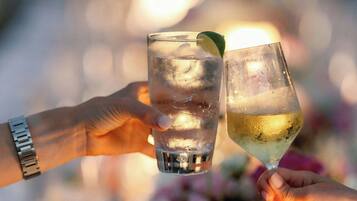 Two hands holding glasses of a beverage, with a blurred background of a table setting and flowers.