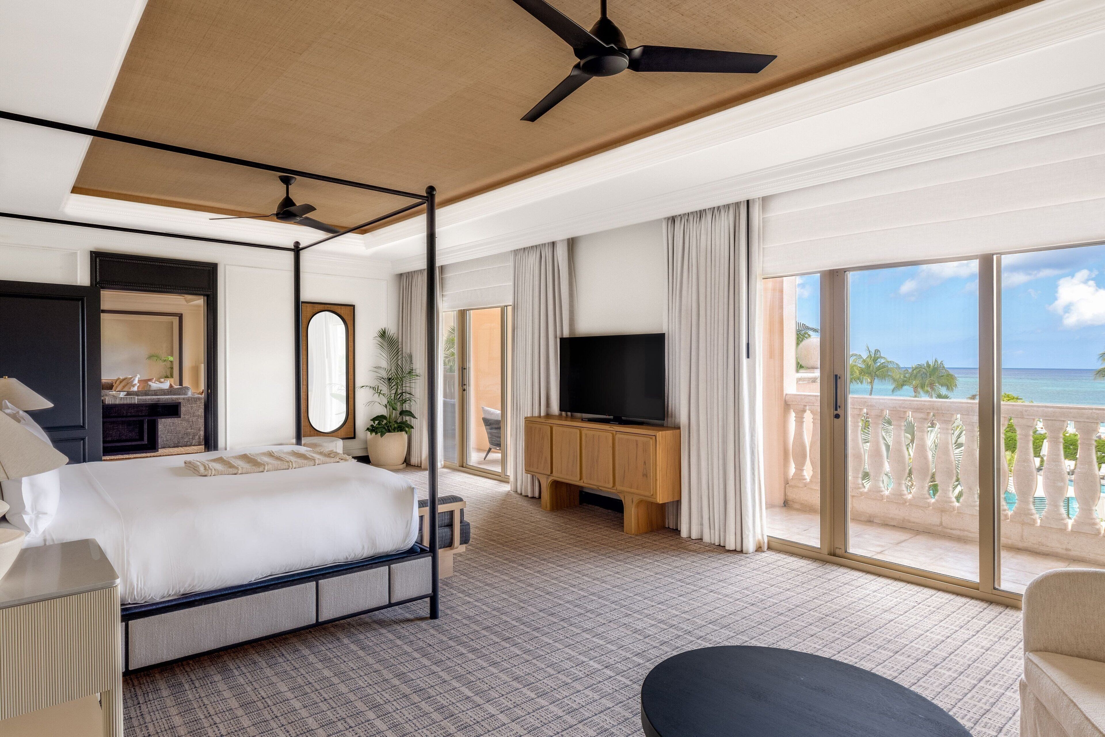 Una camera d'albergo con un letto grande, una TV, un balcone vista mare e una ventola a soffitto.
