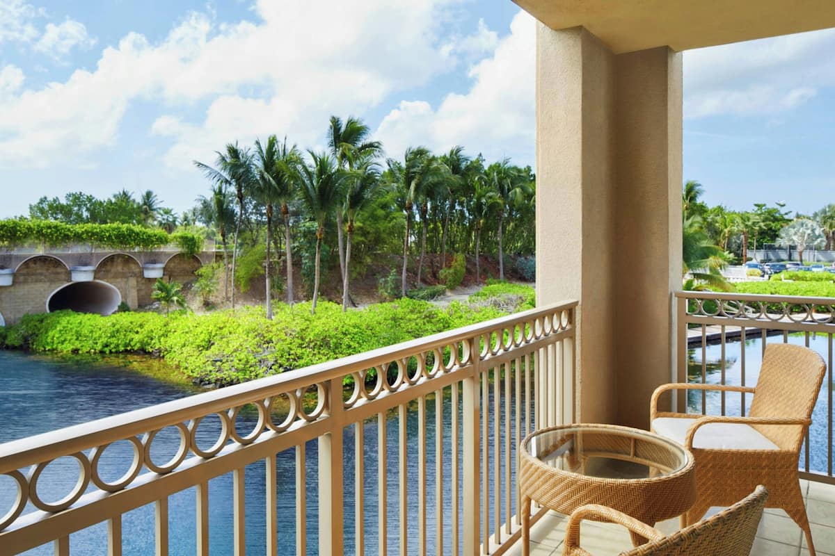 A balcony with wicker furniture overlooking a body of water and palm trees.
