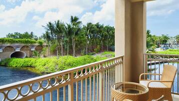 A balcony with wicker furniture overlooking a body of water and palm trees.