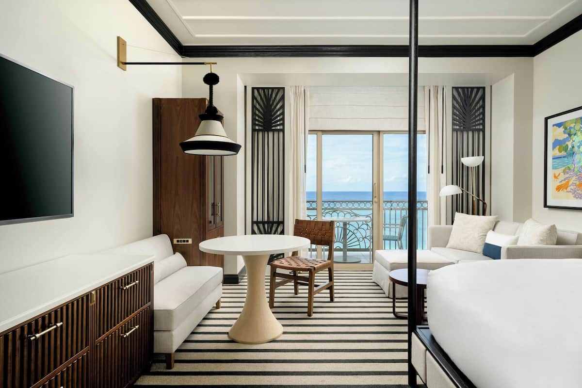 A modern hotel room with a large bed, a sofa, a dining table, and a TV.
