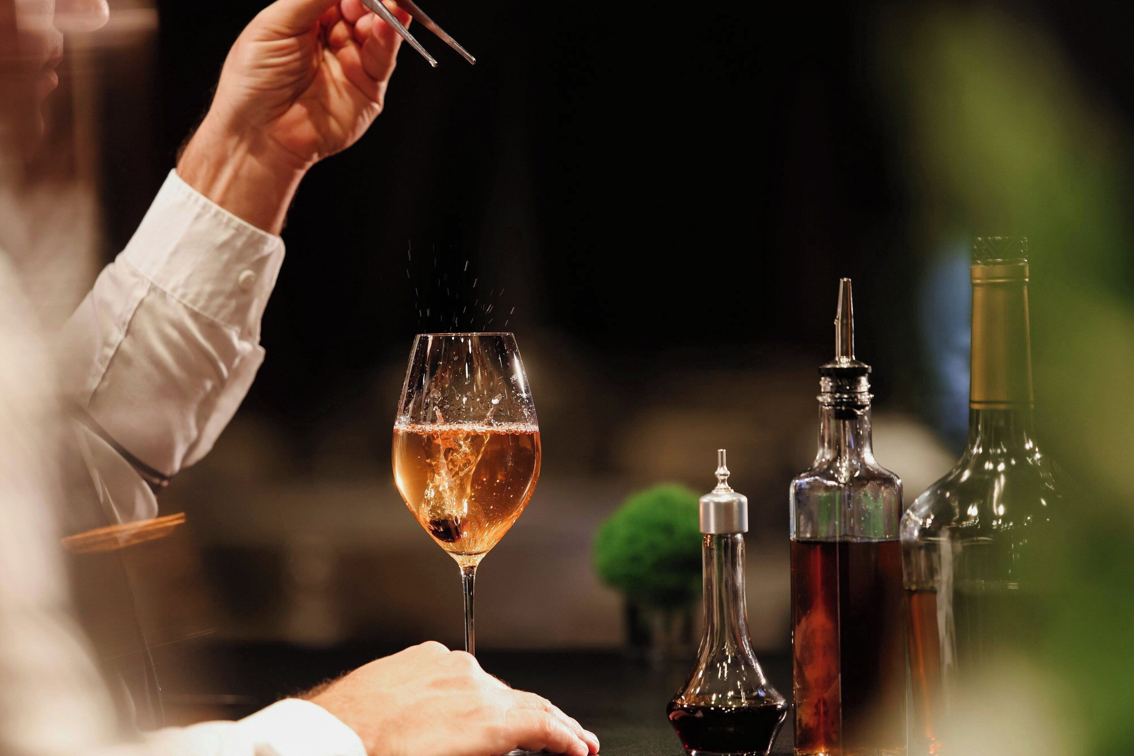 A person holding a glass of wine with a bottle and a decanter on a table.