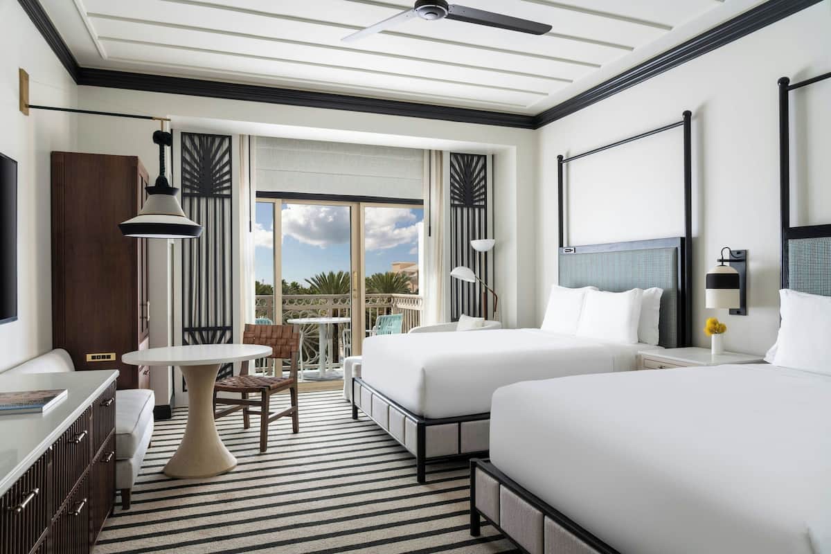 A hotel room with two beds, a dining table, a chair, and a balcony with a view.