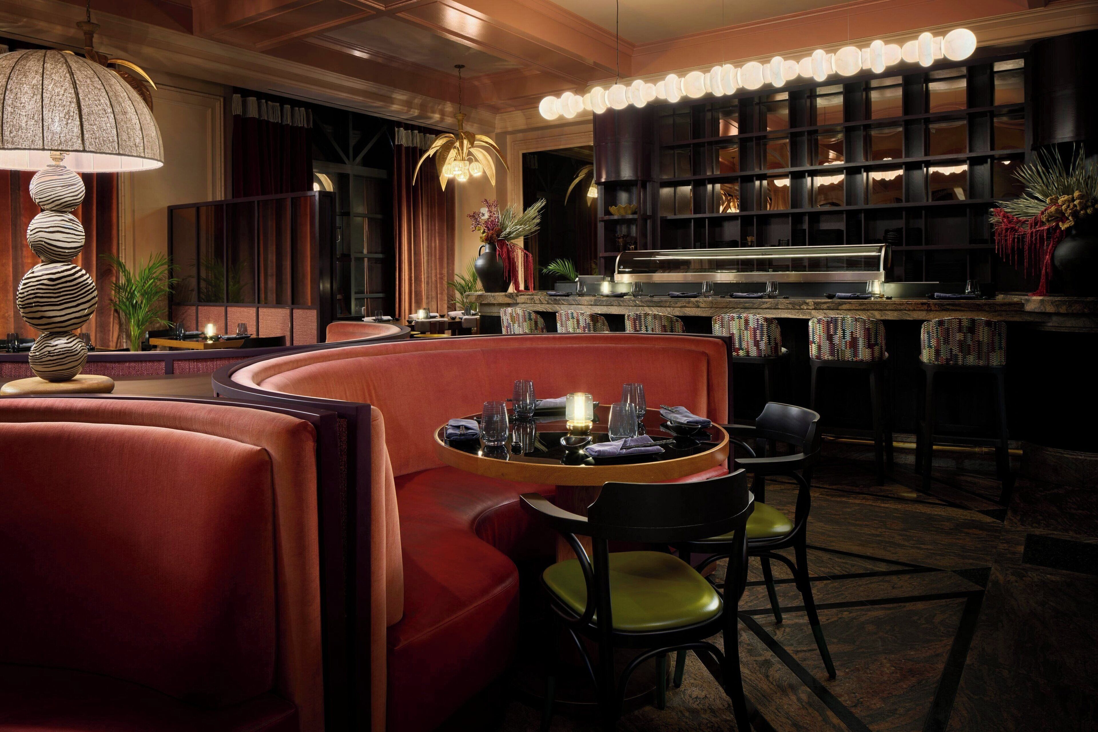 A dimly lit bar area with a round table, red seating, and a bar counter.