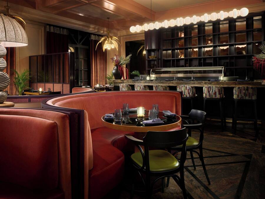 A dimly lit bar area with a round table, red seating, and a bar counter.