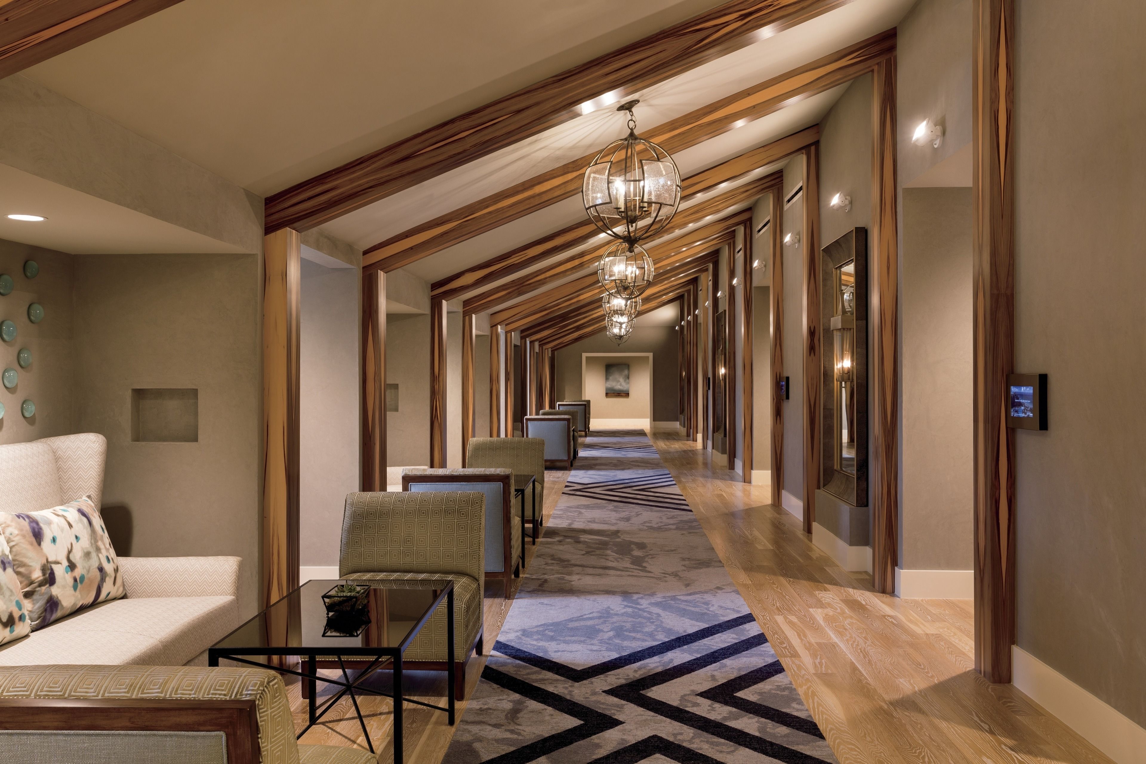 A hotel corridor with a patterned carpet, wooden paneling, and a chandelier.