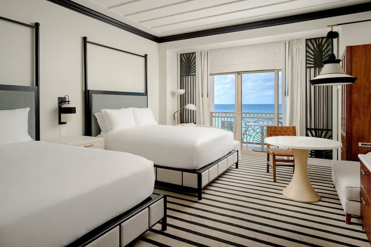 A hotel room with two beds, a dining table, and a view of the ocean.