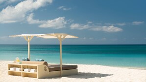 A beachside lounge with a cushioned seating area, a small table with a pitcher, and a canopy umbrella.