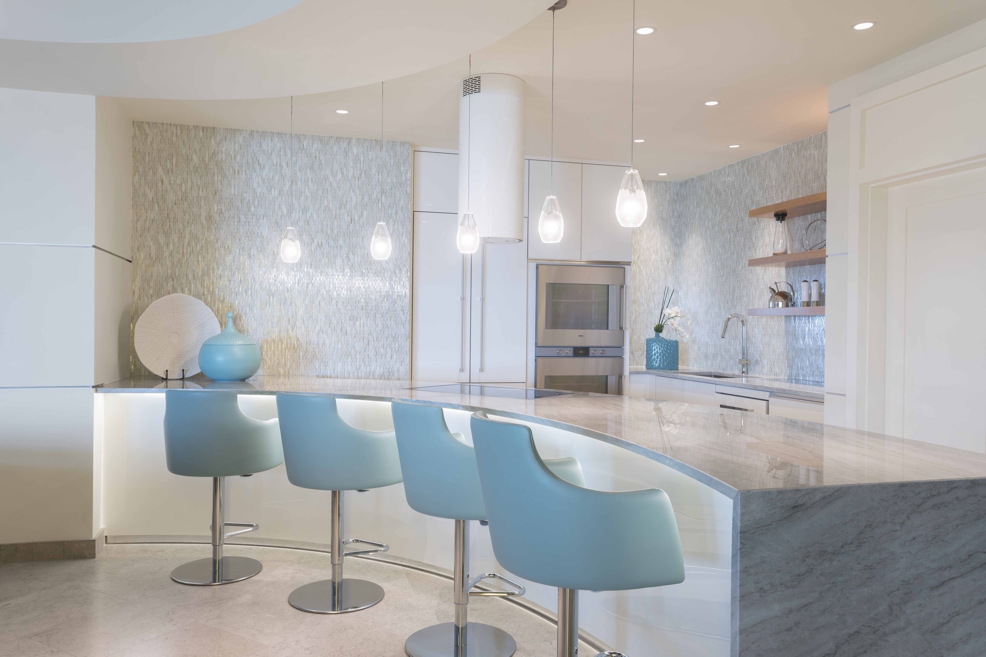 Una cocina moderna con una isla curva, taburetes de bar, iluminación colgante y encimera de mármol.