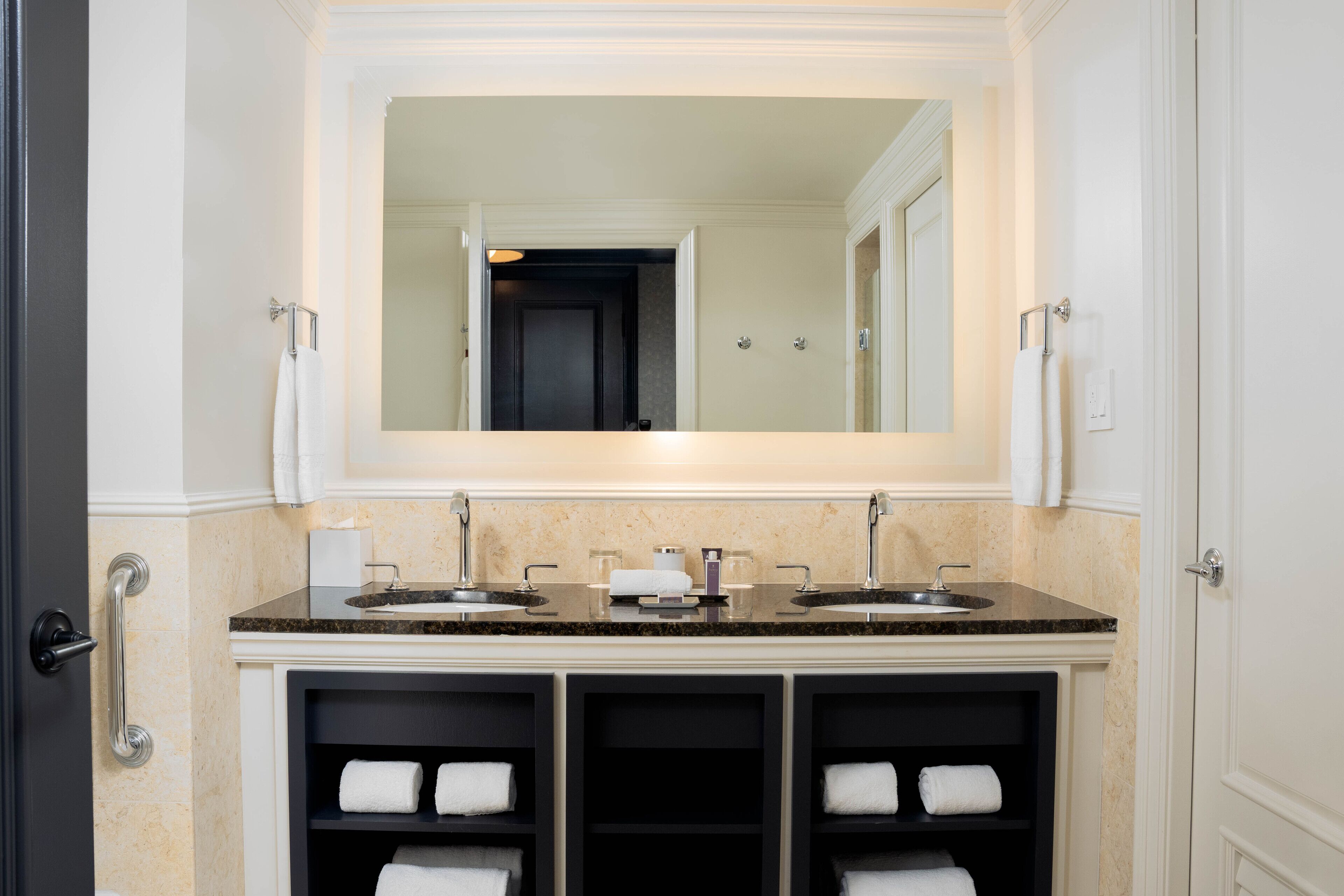 A bathroom with a double sink vanity, a large mirror, and built-in shelves for towels.