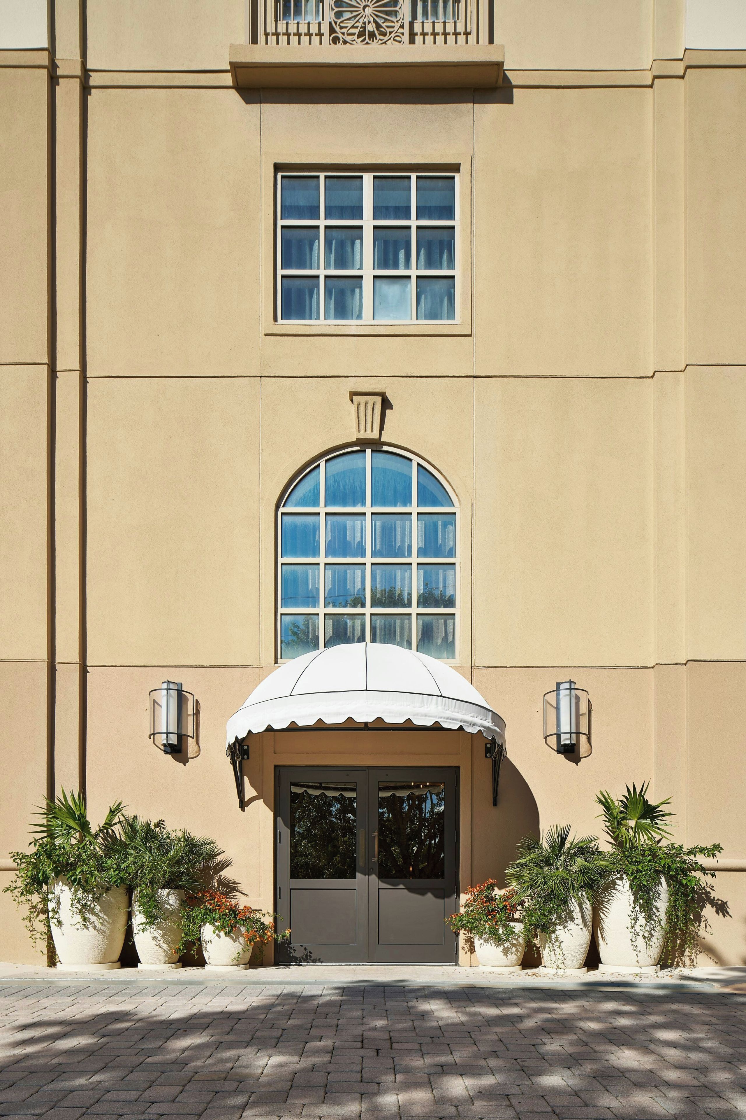 A building with a large arched window, a covered entrance, and potted plants.