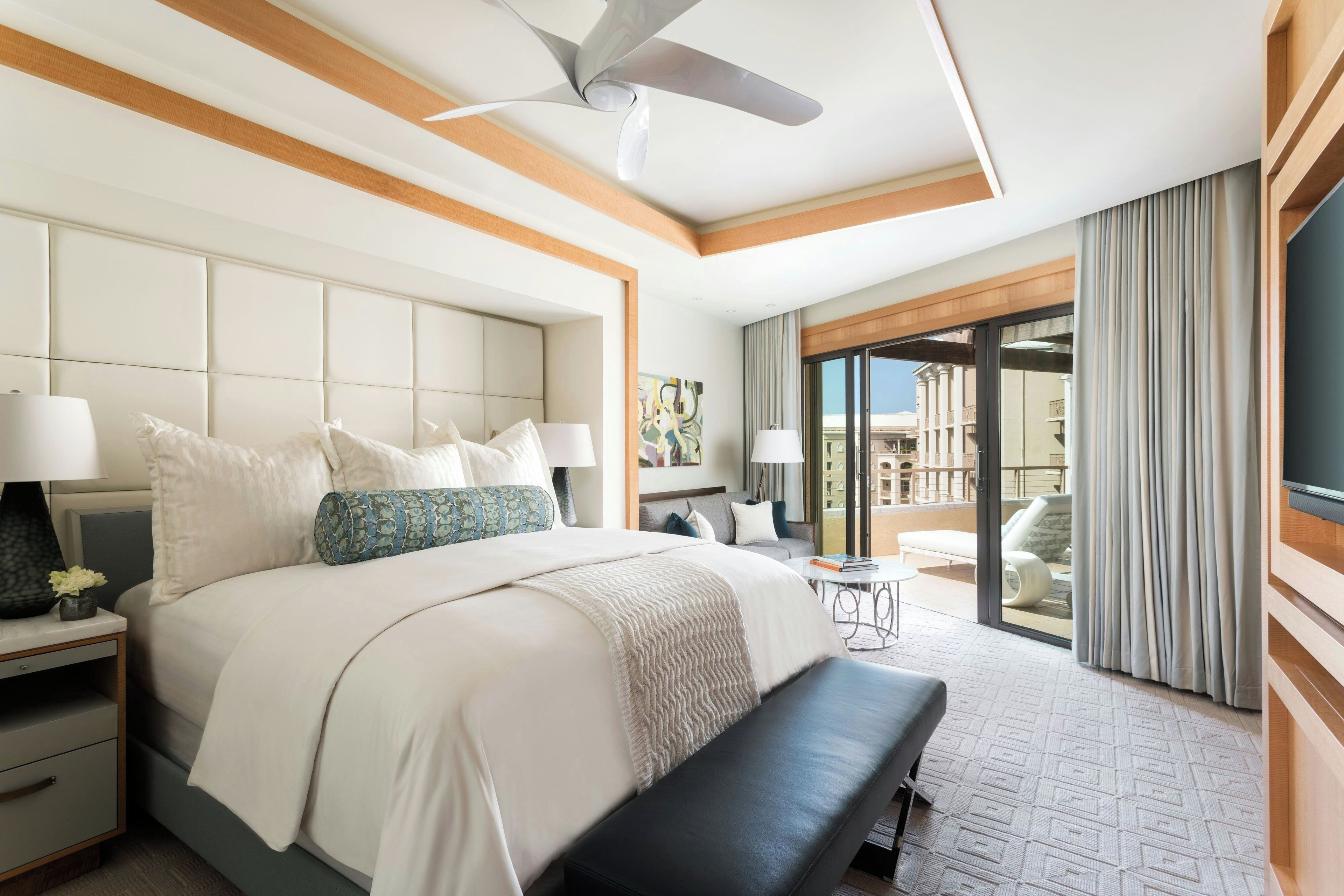 A hotel room with a large bed, a ceiling fan, a balcony with a view, and a TV mounted on the wall.